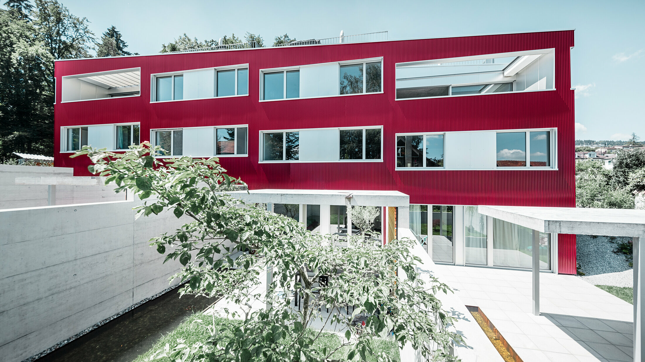 Wohnhausanlage mit Flachdach und Balkonen mit weinroter Fassade mit PREFA Profilwelle 