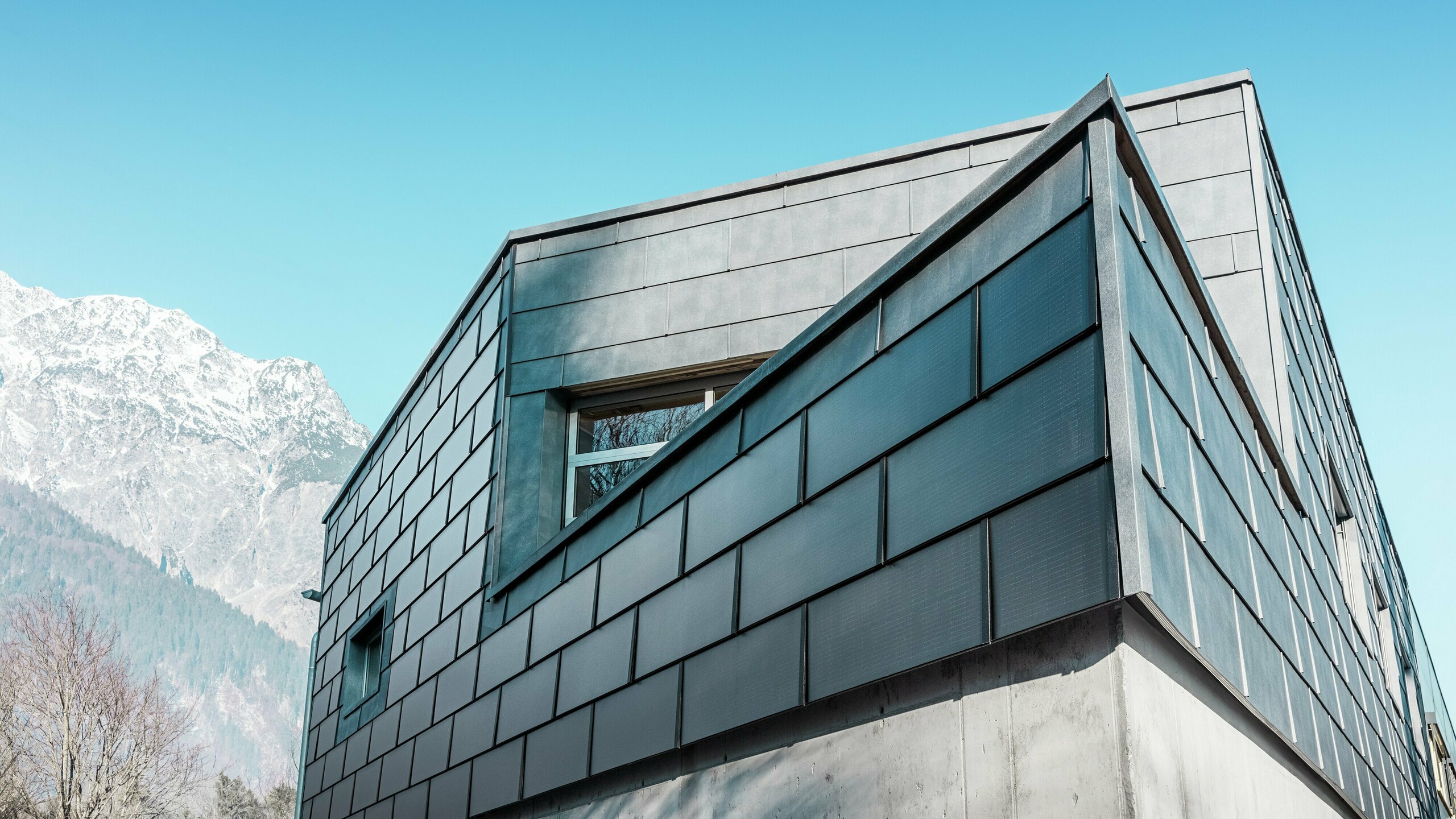 Moderne Fassade mit der PREFA Solardachplatte: Die nachhaltigen Aluminiumplatten mit integrierter Photovoltaik erzeugen Strom und fügen sich harmonisch in das architektonische Design ein.