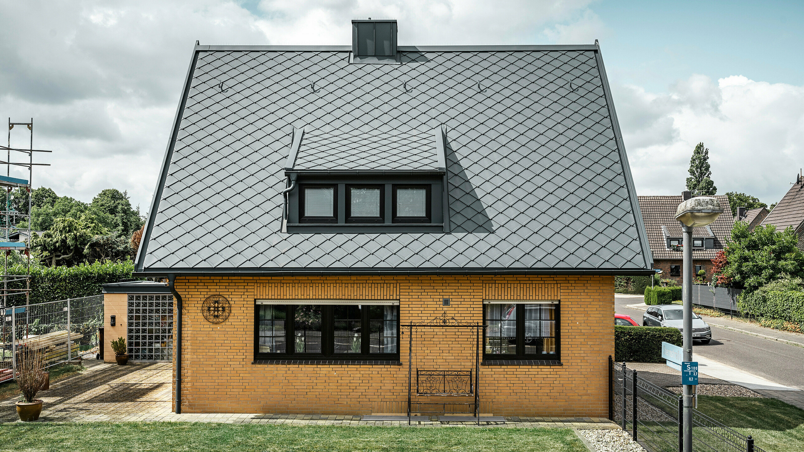 Detached home in Tönisvorst Seitenansicht eines Einfamilienhauses in Tönisvorst mit einem anthrazitfarbenen PREFA Dach aus Dachrauten 29×29. Die Kombination des traditionellen gelben Backsteins mit den modernen Dachelementen und Zubehör aus Aluminium ergibt ein harmonisches Gesamtbild. Schleppgauben und Kamin, ebenfalls in Anthrazit gehalten, vervollständigen das ästhetische und funktionale Dach in einer kleinstädtischen Umgebung.