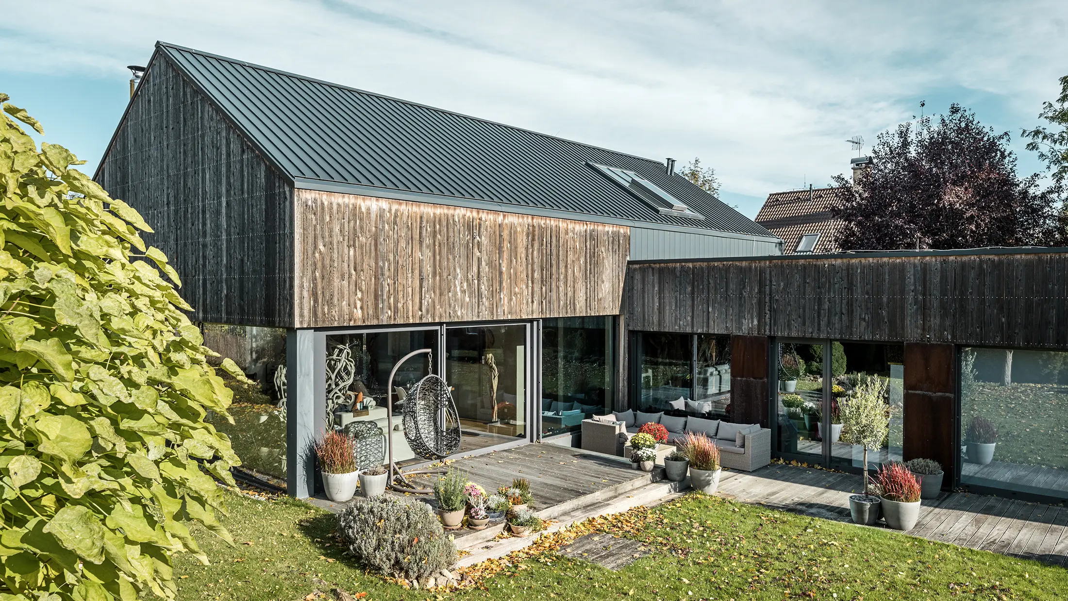 Einfamilienhaus in CZ mit Satteldach aus Aluminium. Das Dach wurde mit PREFALZ Doppelstehfalz in P.10 Anthrazit eingedeckt und mit einer Fassade aus verwittertem Zedernholz versehen. Die schöne Holzterrasse und die großzügigen Fensterflächen im Erdgeschoss unterstreichen den modernen Charakter.
