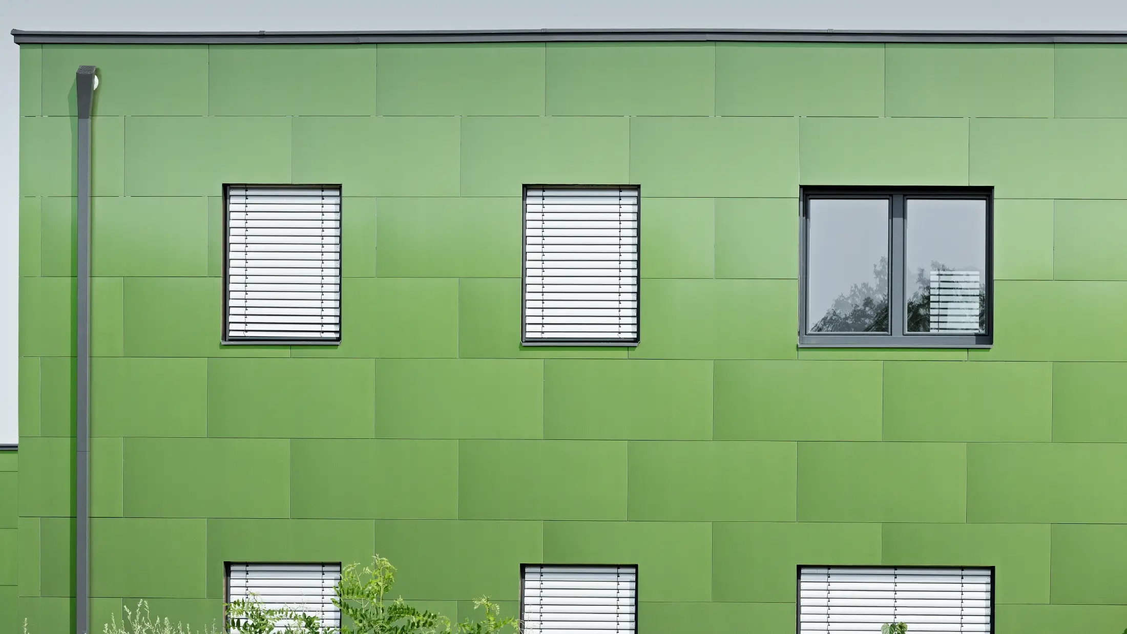 Frontalni pogled na PREFA aluminijumski kompozitni panel s kameleonskim efektom i promenljivim bojama. Sasvim levo vidi se četvrtasta olučna cev kompanije PREFA