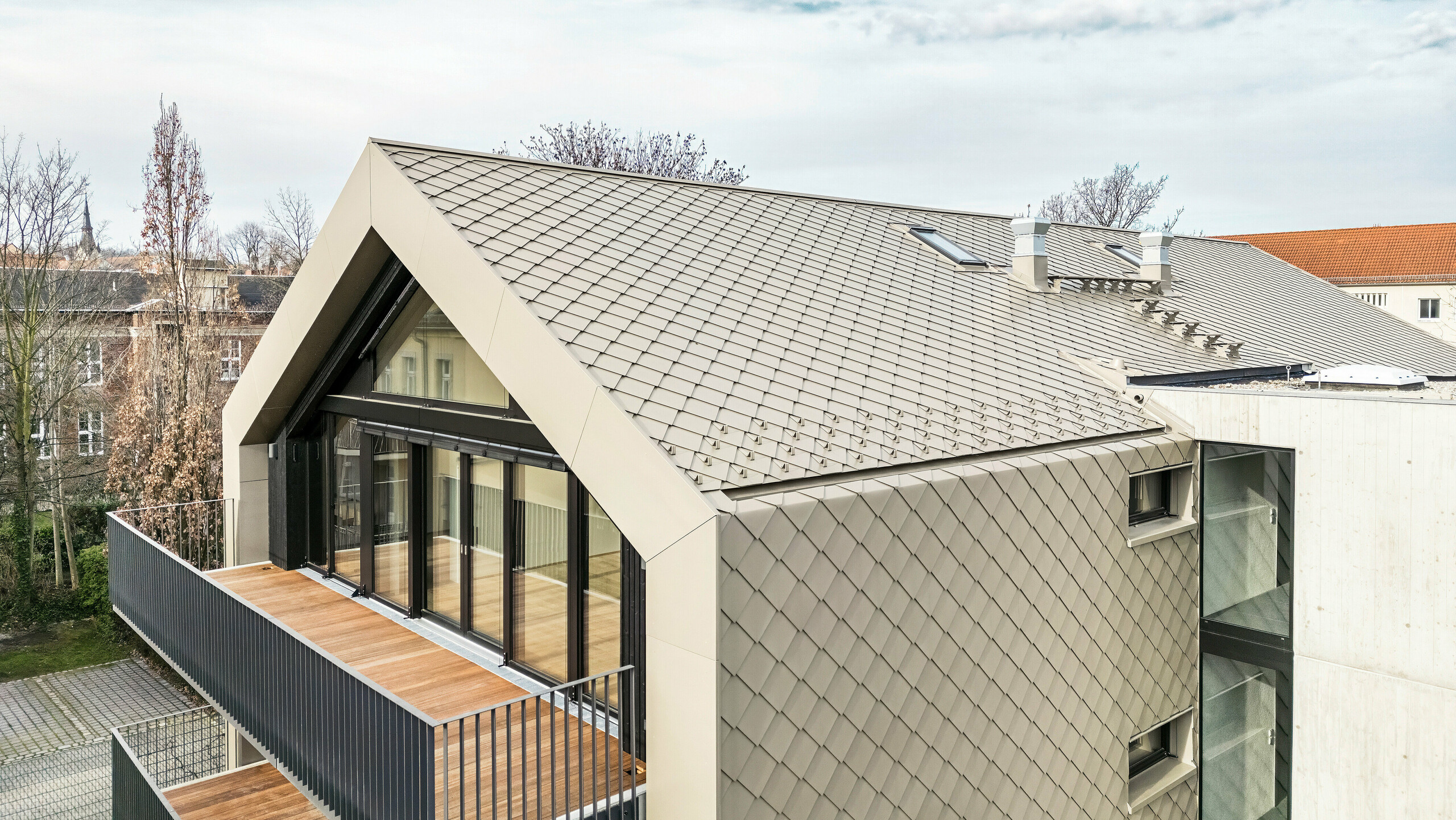 Apartment building in Dresden Vogelperspektive auf ein modernes Mehrfamilienhaus in der Chemnitzer Straße (Dresden) mit einer Gebäudehülle aus PREFA Aluminium-Rauten 29 × 29 in Bronze. Das Bild zeigt die elegante Dachstruktur, die großen Glasfronten und Balkone sowie die harmonische Integration des Gebäudes in die Umgebung. Die hochwertigen Materialien unterstreichen die langlebige Architektur des Gebäudes.
