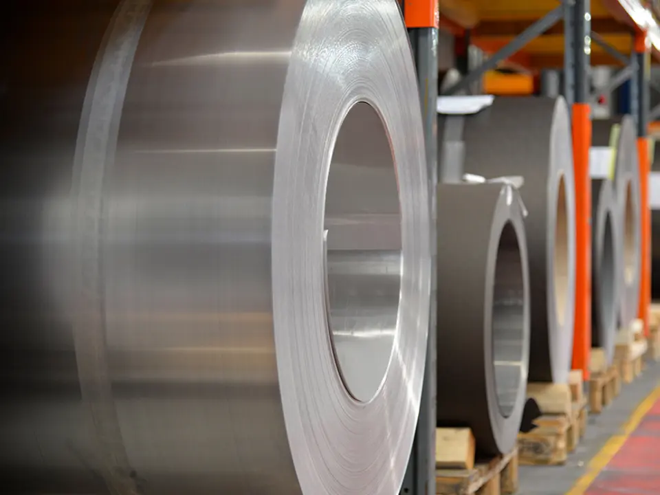 Aluminiumrollen (Coils) gelagert auf Holzpaletten, im Vordergrund steht eine naturblanke Alurolle, dahinter findet man weitere Bänder und Bleche aus Aluminium.