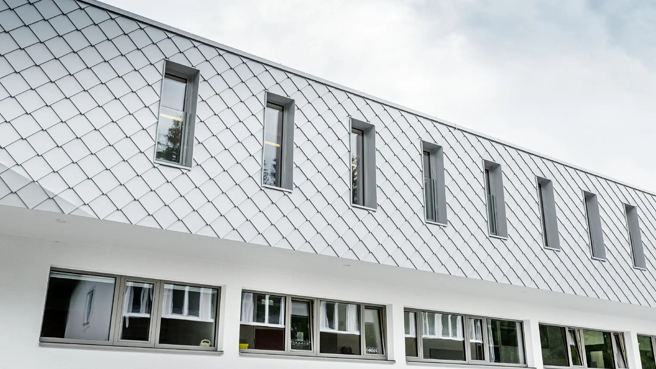 Novoizgrađeni vrtić u Kaprunu sa modernom aluminijumskom fasadom obloženom PREFALZ zidnom rombom u Prefa beloj boji