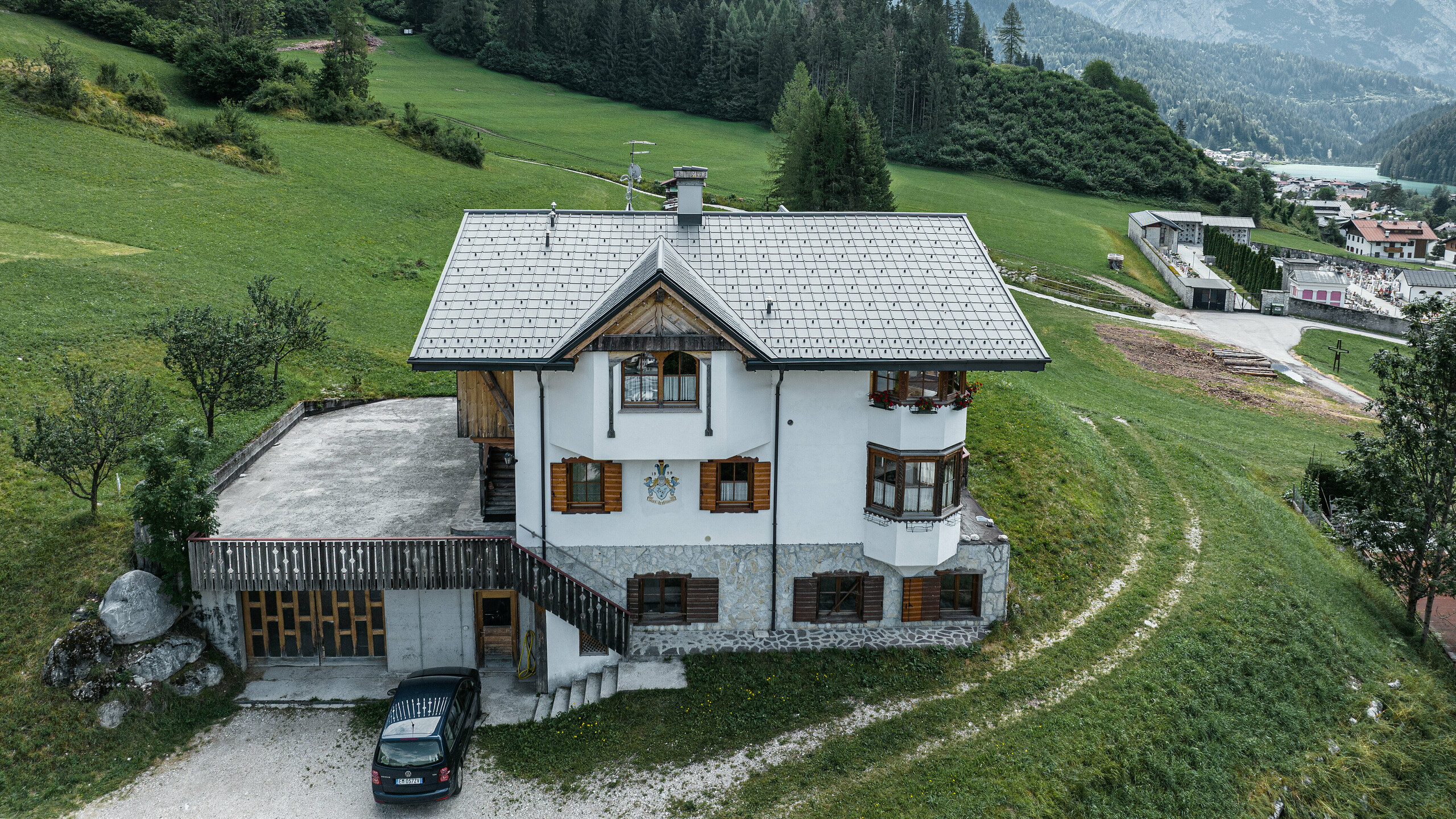 Mountain hut with PREFA roof tile in the colour P.10 light grey Blick aus der Vogelperspektive auf den Eingang der traditionellen Berghütte in Auronzo di Cadore nach der Dachsanierung mit PREFA Ziegeln aus Aluminium in P.10 Hellgrau. Das Gebäude mit seinem charakteristischen alpinen Charme und dem modernen Blechdach fügt sich harmonisch in die üppig grüne Landschaft und das beeindruckende Bergpanorama im Hintergrund ein und demonstriert eine gelungene Kombination aus Funktionalität und regionaler Architektur.