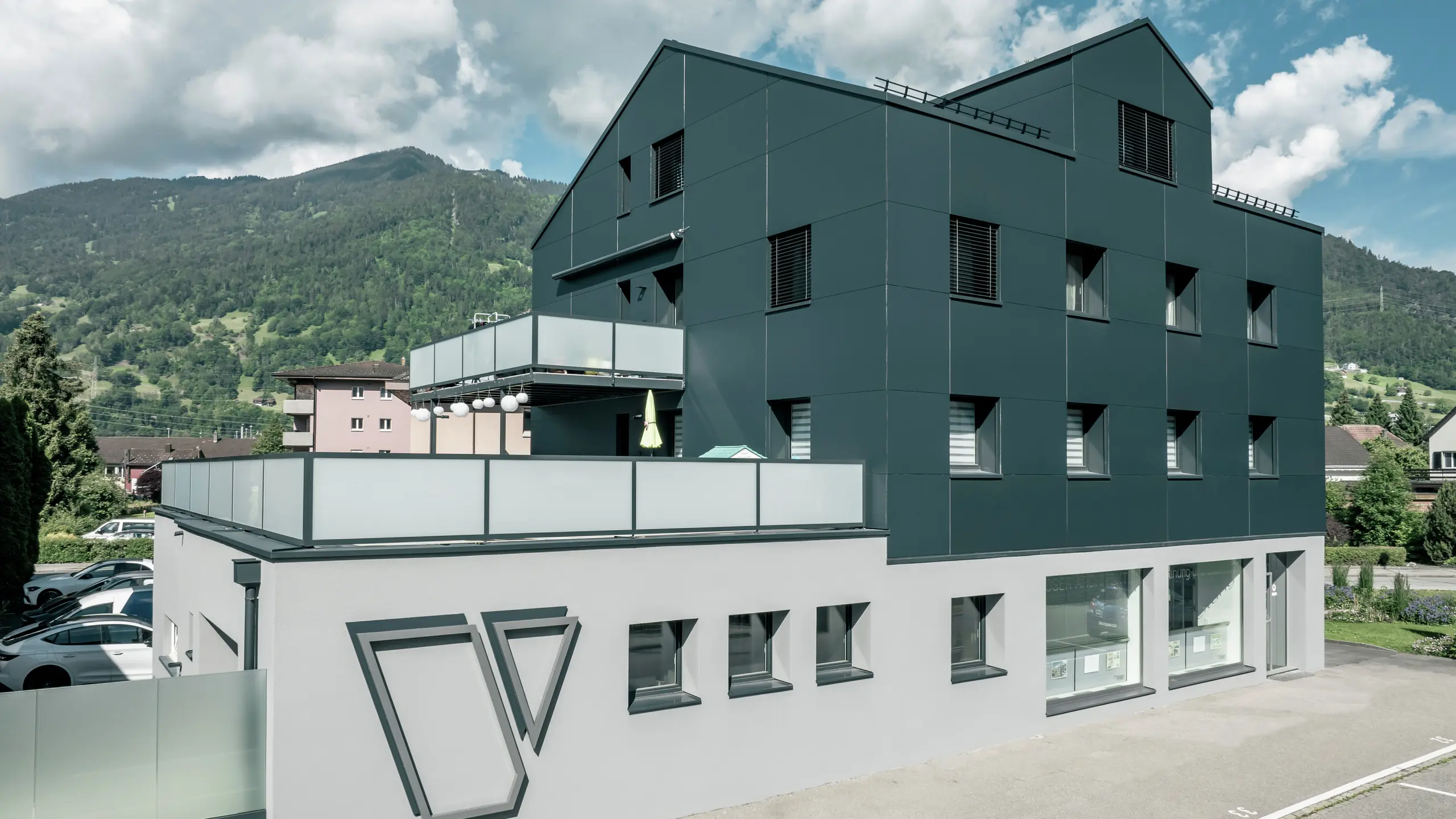 Arhitektonska firma Voser u Landkvartu, u švajcarskom kantonu Graubinden, odlikuje se PREFA aluminijumskom fasadom u antracit boji. Zgrada je renovirana i opremljena PREFABOND aluminijumskim kompozitnim panelima. Dizajn kombinuje čiste linije i visokokvalitetne materijale. Veliki balkoni sa staklenim balustradama i istaknuti logo Voser na bočnoj strani zgrade su posebno upečatljivi. U pozadini se vidi zeleni planinski pejzaž.