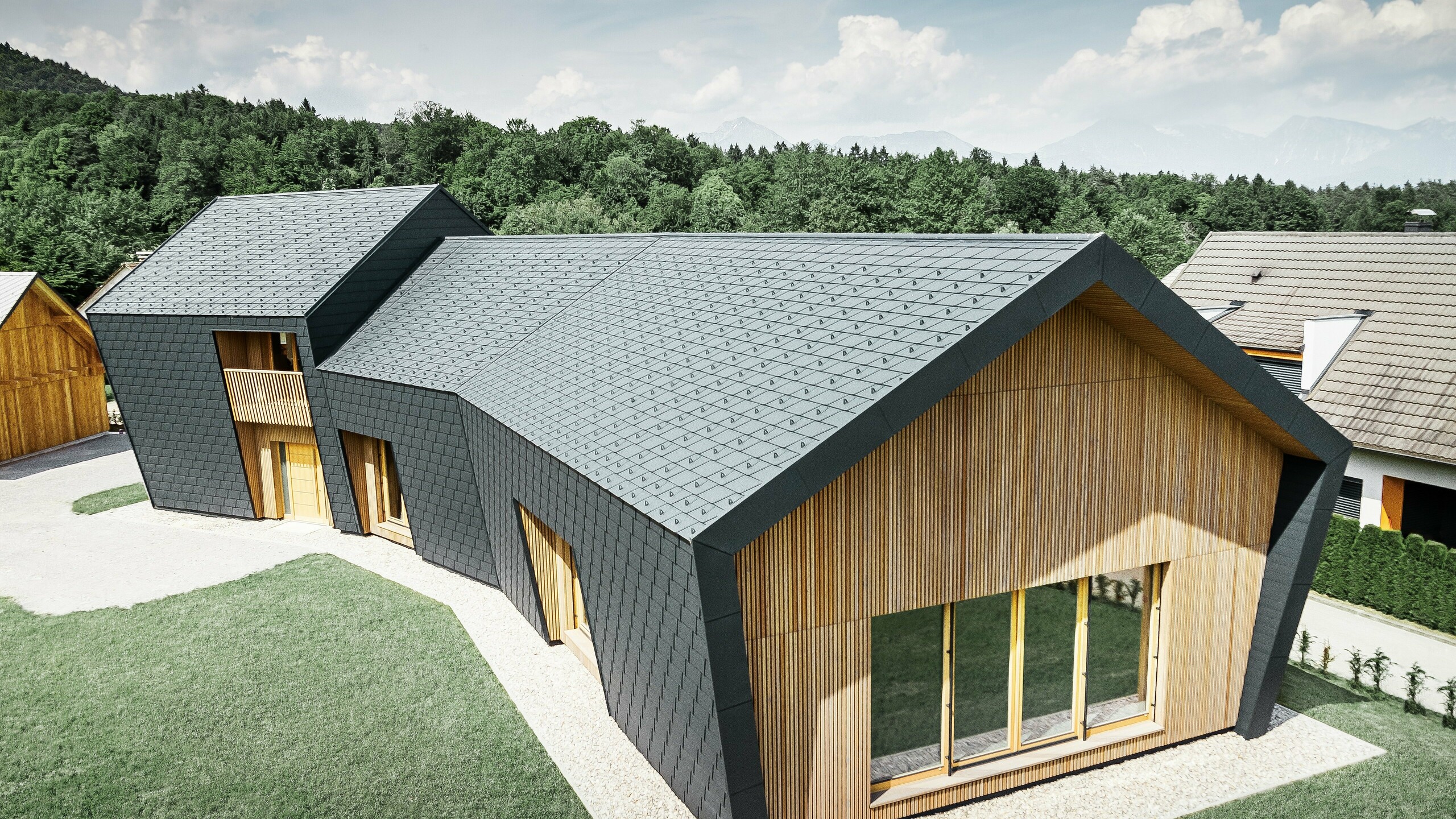 Velike krovne i fasadne površine prekrivene krovnim šindrama DS.19 u P.10 antracit boji, dok je prednja strana fasade obložena drvetom
