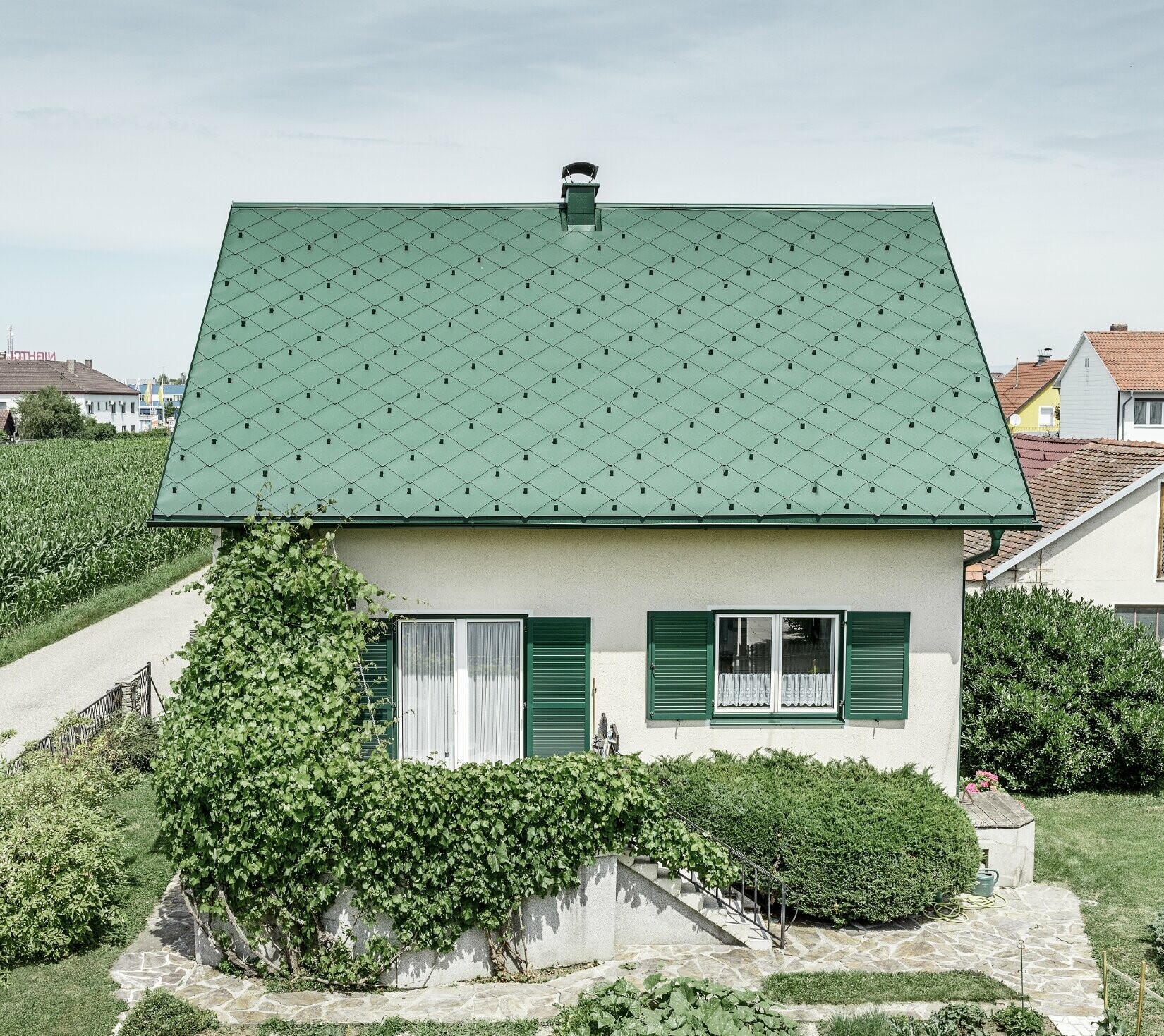 Dachsanierung mit RPEFA Dachraute 44 × 44 in Moosgrün Klassisches Einfamilienhaus mit Satteldach mit einer Dacheindeckung aus Aluminium von in moosgrün mit grünen Fensterläden. Das Dach wurde mit PREFA Dachrauten 44 × 44 in P.10 Moosgrün eingedeckt.