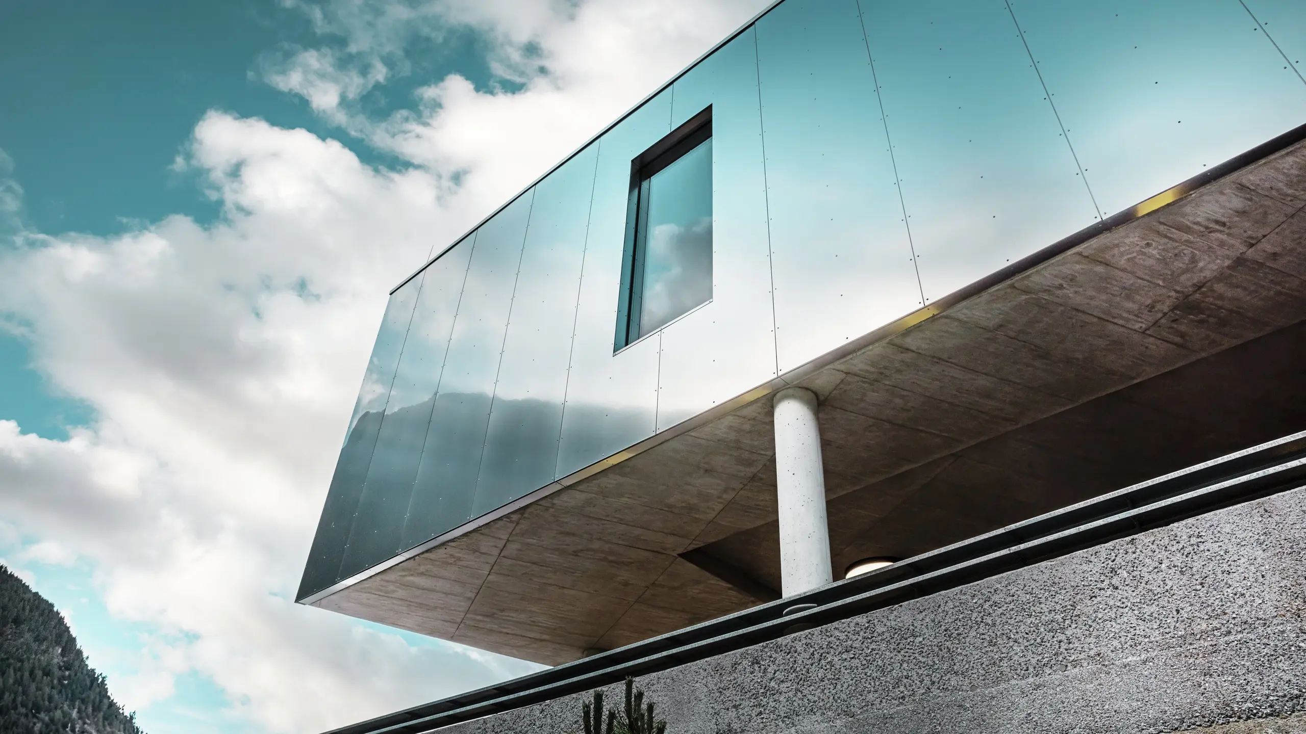 Moderna arhitektura supermarketa MPREIS u Zeldenu, Tirol, sa reflektujućim PREFA aluminijumskim kompozitnim panelima u posebnoj boji Reflective Natural. Sjajna fasada reflektuje nebo i planinski pejzaž. Čiste linije i čvrsti betonski stubovi kombinuju inovativni dizajn sa stabilnošću i elegancijom.