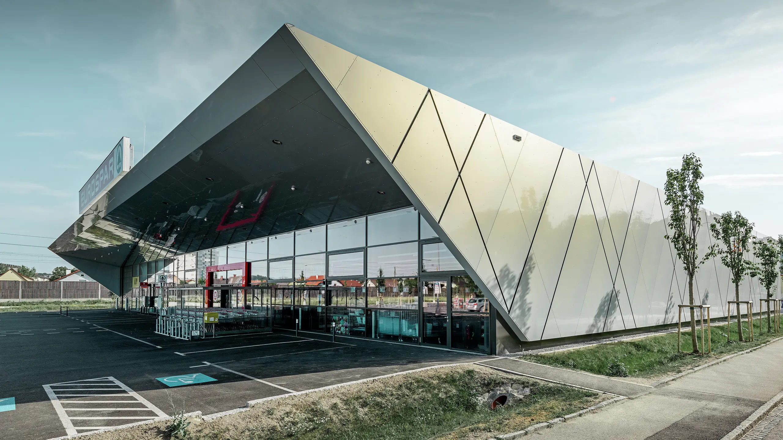 Ulazni deo supermarketa EUROSPAR kombinuje prostrane staklene površine sa upečatljivom PREFA aluminijumskom fasadom. Sjajna površina posebne srebrno-zlatne boje ističe visokokvalitetnu, ka budućnosti orijentisanu arhitekturu filijale supermarketa. Aluminijumski kompozitni paneli svetlucaju na sunčevoj svetlosti, prikazujući različite boje u zavisnosti od ugla gledanja.