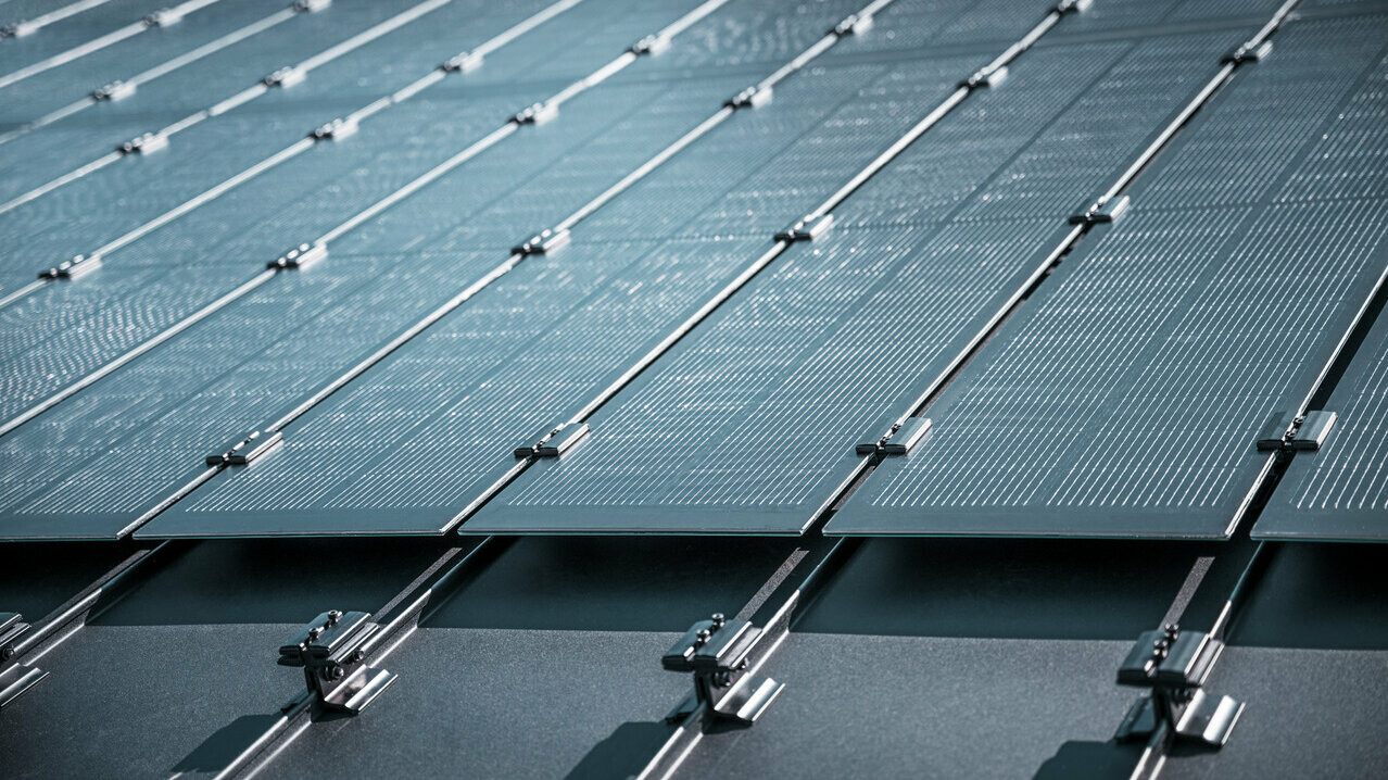 Montageansicht mehrerer PREFALZ Solarmodule auf einem bestehenden PREFALZ Dach in Meschede, Deutschland. Die rahmenlosen Glas/Glas-PV-Module sind in präzisen Reihen angeordnet und mit robusten Halterungen fixiert, was eine flächenbündige, elegante Optik erzeugt. Die hochwertige Befestigungstechnik sorgt für Stabilität und Langlebigkeit, während die innovative TOPCon-Zellentechnologie maximale Energieeffizienz garantiert. Das Bild vermittelt modernste Photovoltaik-Lösung, die Design, Funktionalität und Nachhaltigkeit perfekt vereint.