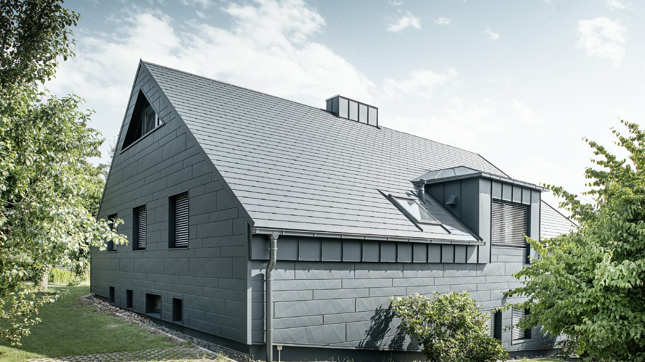 Großes Einfamilienhaus mit Satteldach und vielen Fenstern. Das gesamte Haus wurde mit einer Aluminiumhülle in Anthrazit verkleidet, am Dach kamen PREFA Alu-Dachschindeln zum Einsatz und an der Fassade Siding.X in Anthrazit.
