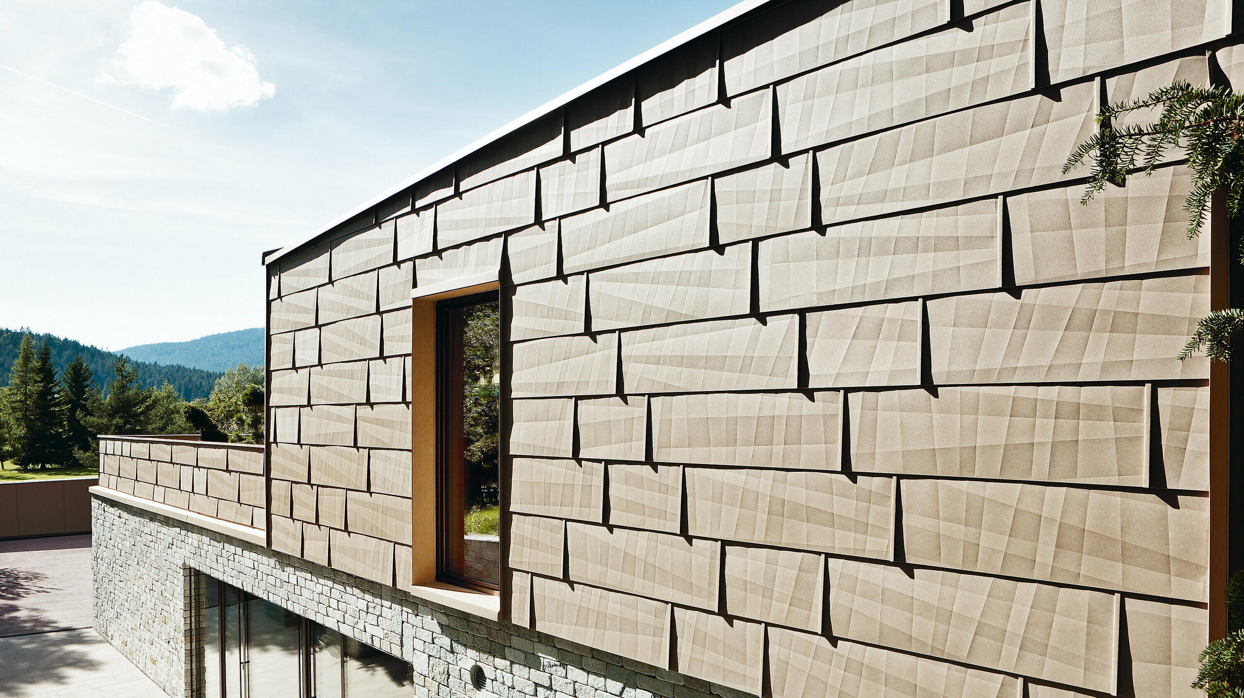 Na ovoj spoljašnjoj fasadi kombinovan je PREFA fasadni panel FX.12 u boji P.10 pesak bež sa kamenom fasadom u prizemlju.