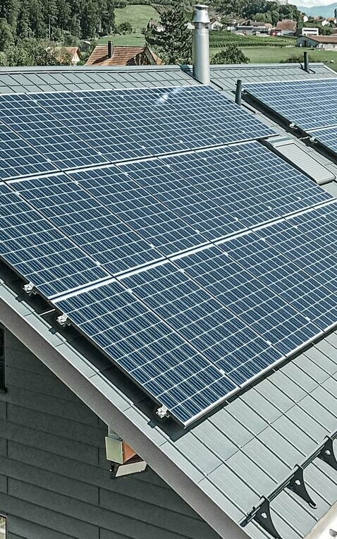 Das Bild zeigt ein modernes Einfamilienhaus mit mehreren PREFA Aluminiumprodukten. Die große Photovoltaikanlage (PV-Anlage) auf dem Dach verdeutlicht den Wert von nachhaltiger Stromerzeugung. Die PV-Module sind sorgfältig auf der gesamten Dachfläche installiert, um maximale Sonnenenergie zu nutzen. Zusätzlich ist ein Schneeschutzsystem integriert, das speziell für die Kombination mit Energiegewinnungsflächen entwickelt wurde. Dieses System verhindert das Abrutschen von Schnee und sorgt so für Schutz vor Dachlawinen. Auf dem Dach des Gebäudes wurde die bewährte PREFA Dachplatte in der Farbe Anthrazit verlegt. Das robuste Dachsystem aus Aluminium ist besonders langlebig und robust. Der Giebel des Hauses wurde mit hochwertigen PREFA Sidings in der gleichen Farbe verkleidet. Die Kombination der hochwertigen Blechverkleidungen bietet starken Schutz und eine eindrucksvolle Optik.