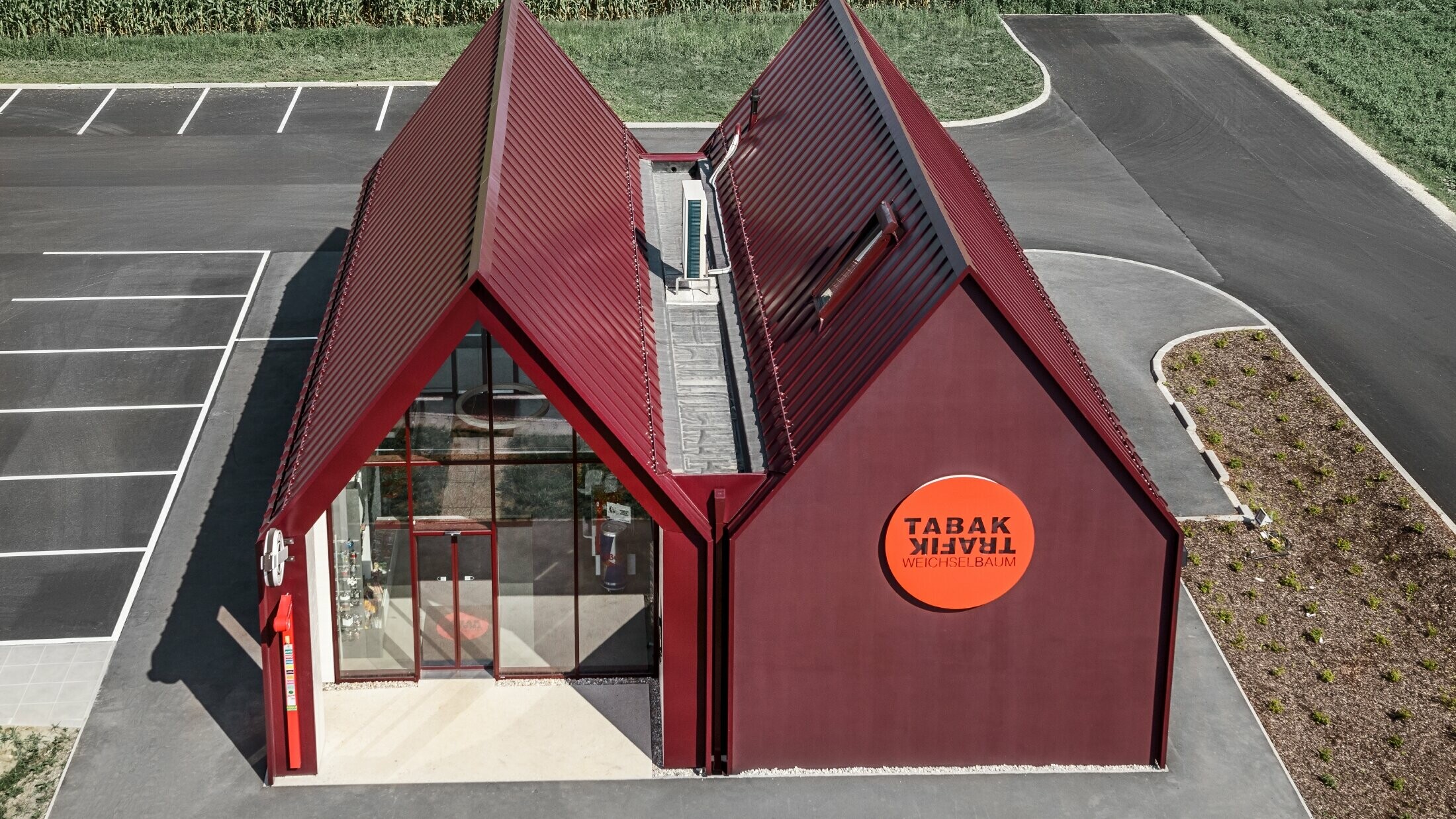 Modern tobacconist's in St. Valentin, PREFALZ in special black-red colour moderne Trafik mit Satteldach und ohne Dachvorsprung und einer Aluminiumhülle von PREFA als Stehfalz- und Winkelstehfalz in der Sonderfarbe schwarzrot ausgeführt